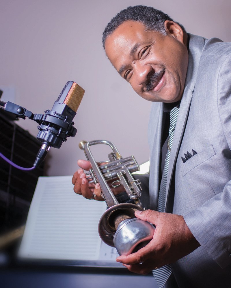 William Bill McGee holding a trumpet beside a studio microphone