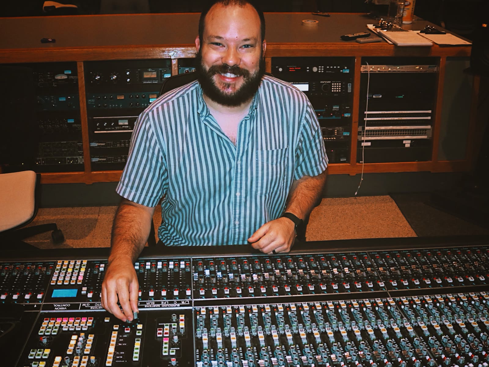 Dustin Painter smiling behind a large-format audio mixing console